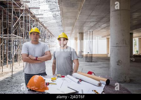 Confident teams of architect, Engineer, Contractor, or Construction manager standing side by side in front of a desk at a construction site. Stock Photo