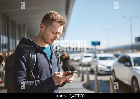 Man holding smartphone and using mobile app against a row of taxi cars. Themes modern technology, carsharing and travel. Stock Photo