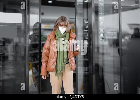 Woman in mask going out from shop with a coffee cup Stock Photo