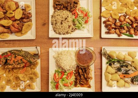 Dining table with square plates with Dominican recipes of grilled fish with boiled potatoes, with slices of plantain, chicken mince, picatodo, Moorish Stock Photo