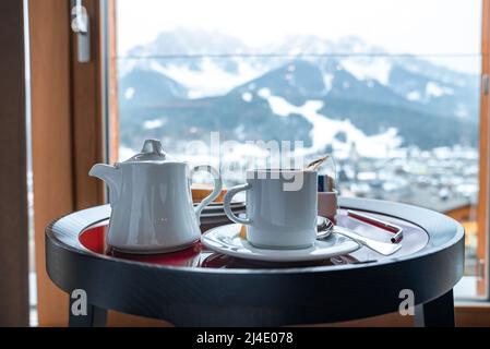 White tea pot and cup with breakfast on table against mountains in background Stock Photo