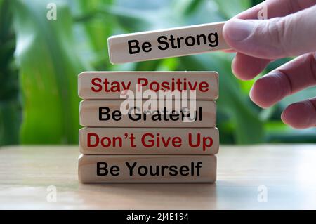 Self-help motivational text on wooden blocks with hand holding a wooden block and blurred nature background. Stock Photo