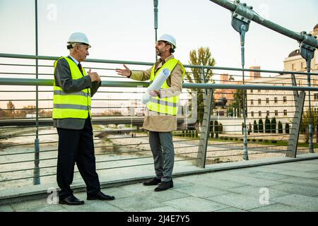 Two senior construction managers are standing on the bridge while talking about the new plans and ideas Stock Photo