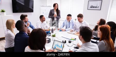 Group Of Smiling Young Multi Ethnic Businesspeople Looking At Businesswoman Giving Presentation In The Meeting Stock Photo
