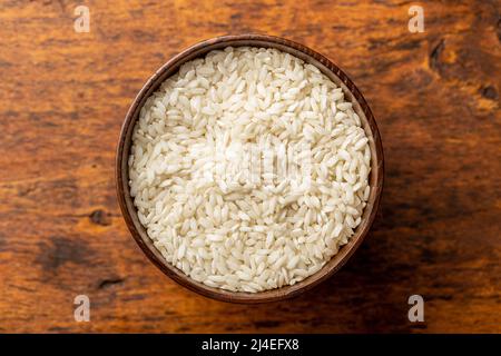 Uncooked Carnaroli risotto rice in bowl on a wooden table. Top view. Stock Photo