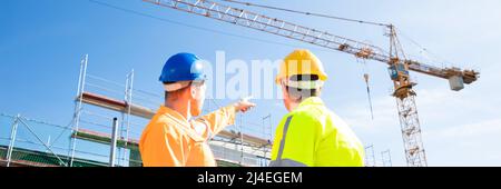 Rear View Of Two Male Architect Wearing Hardhat Looking At Construction Site Stock Photo