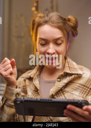 Macro shot. Girl gamer with a portable game console. Playing a video game online with friends. Emotionally reacts to the game. Communication, prizes, Stock Photo