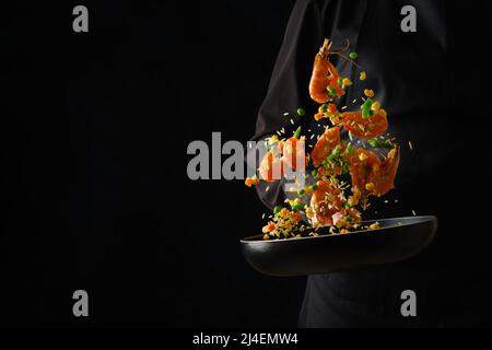 Colorful assorted seafood and vegetables in a frying pan in a frozen flight in the chef's hand. Isolated on black background. Food for gourmets. Resta Stock Photo