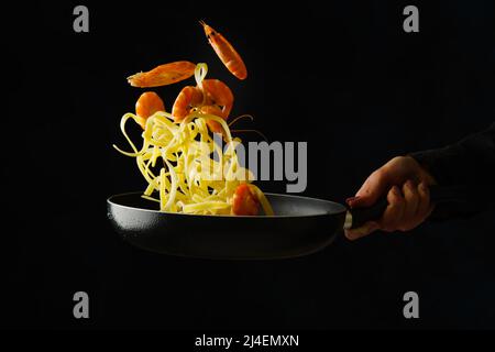 Professional chef prepares pasta, spaghetti with shrimps on a black background. Frozen in-flight food. Healthy vegetarian food, healthy lifestyle, org Stock Photo