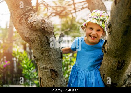 happy little girl climbs a tree in park on sunny summer day Stock Photo