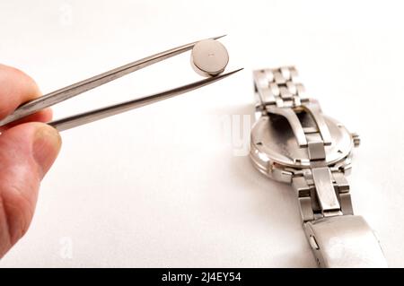 watchmaker is working to replace the battery on an old quartz metal watch in his repair shop, he is holding the new battery in tweezers and getting re Stock Photo