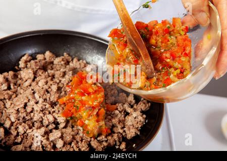 Preparation of ground beef with the traditional Colombian hogao or criollo sauce (salsa criolla) made of onion, tomato, peppers and cilantro Stock Photo