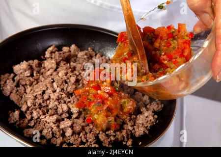 Preparation of ground beef with the traditional Colombian hogao or criollo sauce (salsa criolla) made of onion, tomato, peppers and cilantro Stock Photo