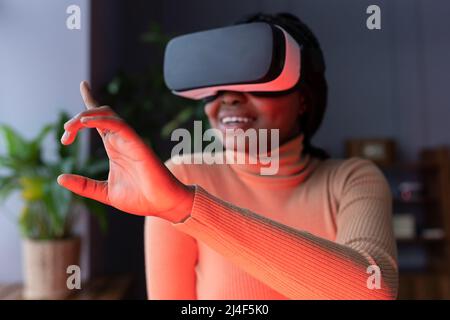 Joyful afro female touching virtual object with finger while working in virtual reality headset Stock Photo