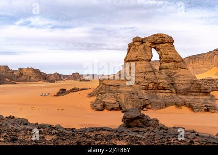 View from Tamesguida cathedral in Tadrart Rouge, Tassili N'Ajjer park.. Far tiny tourists and cars. Natural window rock . Orange color sand and mesa. Stock Photo