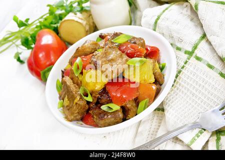 Beef with oranges, bell peppers and ginger root in bowl, a napkin and a fork on white wooden board background Stock Photo