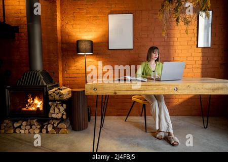 Woman works on laptop in cozy living room with fireplace Stock Photo