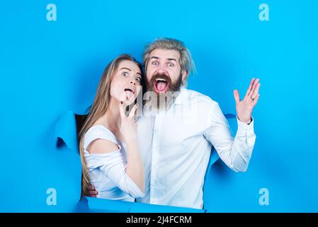 Couple through hole in paper, copy space for text or slogan. Discount and sale, people hole background. Surprised couple, excited face of bearded man Stock Photo