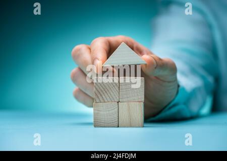 Man's Hand Holding A Roof Of Wooden Block House Stock Photo