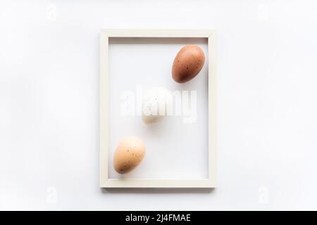 Three natural eco eggs on a white background with copy space for text in a frame. Geometry. Minimal concept. View from above. Easter card, soft select Stock Photo