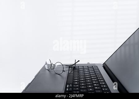 Cropped side view of laptop computer with glasses in light office. Modern workspace of programmer, designer or freelancer. Online remote working Stock Photo