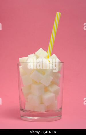 Glass with refined sugar cubes and a drinking tube on a pink background Stock Photo
