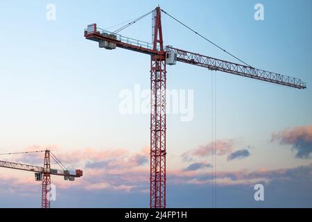 Tall tower cranes on the construction against sunset.  Stock Photo