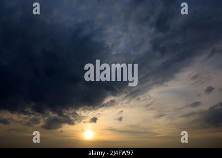 Sky covered with dark storm clouds and setting sun. Dramatic background for weather before rain at sunset Stock Photo