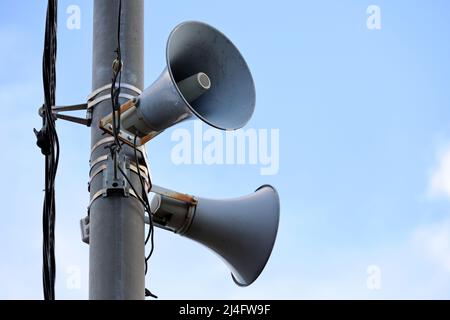 Loudspeakers on pole, alarm siren in city. Two public address system speakers on blue sky background Stock Photo