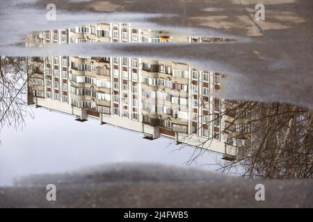 Puddle after rain with reflection of residential building in water. City street at rainy weather in spring Stock Photo