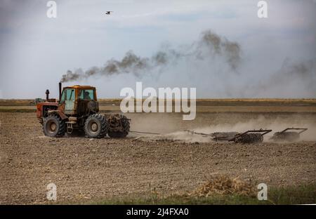 Kyzylorda Province, Kazakhstan - May 01, 2019: Tractor cultivated field soil with plough. Spring sowing season. Stock Photo