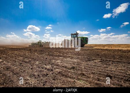 North Kazakhstan Province, Kazakhstan-May 12, 2012: Spring sowing campaign. John Deere tractors cultivating soil with harrow.  Blue sky, clouds Stock Photo