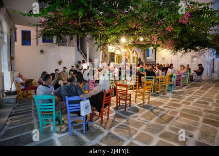 Ios, Greece - June 13, 2021 : Tourists enjoying drinks and listening to live greek music at a picturesque and colorful outdoor bar in Ios Stock Photo
