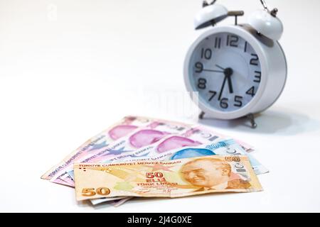 50, 100 and 200 Turkish banknotes and alarm clock on isolated white background. 50 Turkish lira in selective focus. Time is money concept. Stock Photo