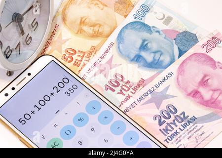 Top view of 50, 100 and 200 Turkish Lira banknotes, alarm clock and calculator app open mobile phone on isolated background. Stock Photo