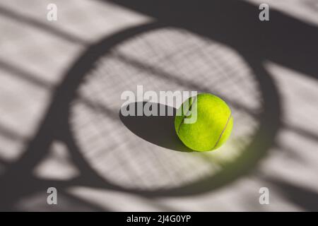 Tennis ball and its shadow on an isolated white background. Tennis ball has tennis racket and net shadow on it. Stock Photo