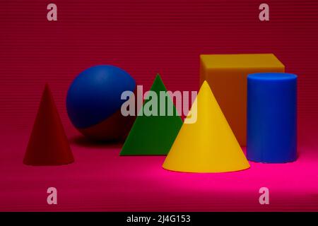 3D different geometric shapes on jagged background in pink hues. Cone with yellow tint in selective focus. Cylinder, triangular prism, cube, cone... Stock Photo