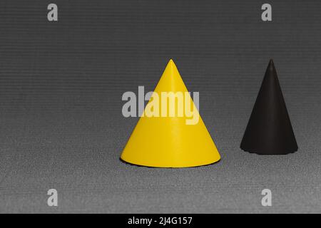 Yellow and black conical geometric shapes on serrated background in gray tones. Yellow cone in selective focus. Stock Photo