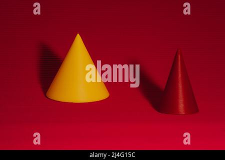Conical geometric shapes on serrated background in red tones. Cone with yellow tint in selective focus. Stock Photo