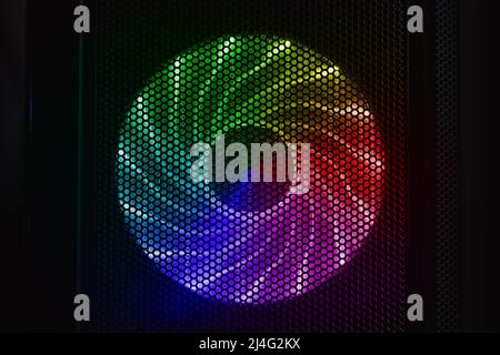 LED lights illuminated PC cooler fan glows with colorful rainbow pattern in dark desktop case, front view Stock Photo
