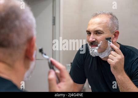 Middle aged handsome man shaving his beard in bathroom Stock Photo