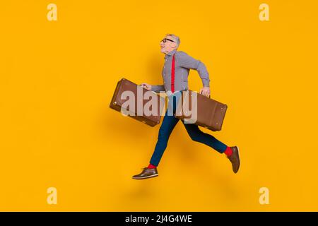 Full size profile side photo of energetic grey haired excited funny pensioner traveling with old valise isolated on yellow color background Stock Photo