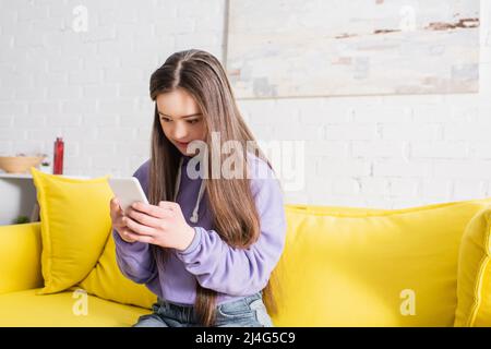 Teen girl with down syndrome using smartphone on couch at home Stock Photo