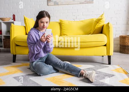 Teen girl with down syndrome using smartphone on floor at home Stock Photo