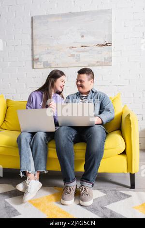 Cheerful teenagers with down syndrome talking using using laptops at home Stock Photo