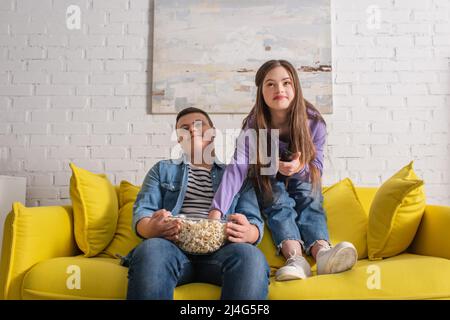 Teenagers with down syndrome holding popcorn while watching tv at home Stock Photo