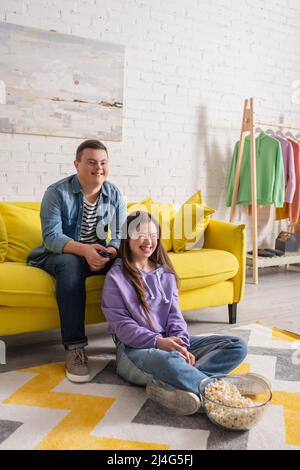 Positive teenagers with down syndrome watching movie near popcorn at home Stock Photo