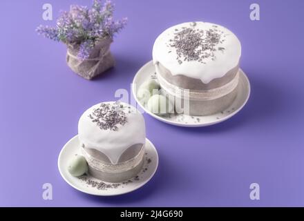 Glazed Easter cakes decorated with lavander flowers and chocolate eggs on bright violet background. Holiday background with copy space for your design. Stock Photo