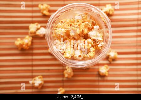 popcorn spilling from a plastic container on wooden background  Stock Photo