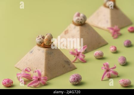 Traditional Easter cottage cheese dessert Paskha decorated with caramel and chocolate candy eggs and spring flowers on pastel green background. Modern minimalistic Easter background with copy space for your design. Stock Photo